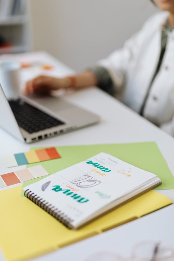 Blurred desk scene with a notebook, color swatches, and a laptop in a modern office.
